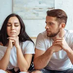 handsome man in jeans and beautiful woman in t-shirt sitting on bed in bedroom