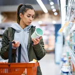 Young woman reading nutrition label while buying diary product in supermarket.