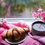 sweet fresh morning coffee and croissant staying on the windowsill with pink flowers