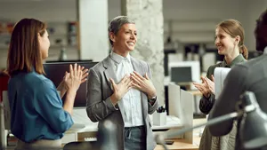 Happy businesswoman feels grateful while group of colleagues are applauding her in office.