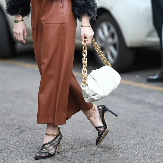 Hoe zwaar mag een handtas zijn? – Streetstyle-foto van vrouw in bruinleren rok met zwarte hakken en witte handtas.