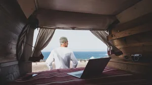 Man kijkt vanuit een camper naar zee, met een open laptop op het bed
