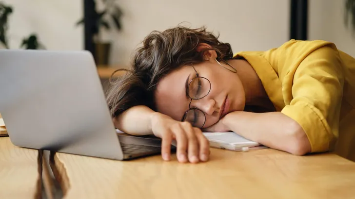 Young tired woman in eyeglasses sleeping on desk with laptop at