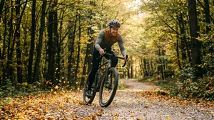 Mannelijke gravelbiker met helm fietst met snelheid door een herfstig bos.