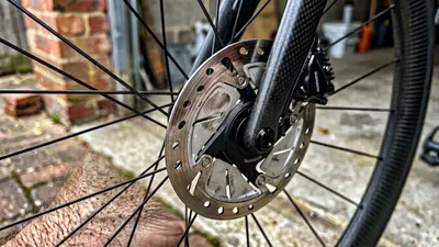 Een gedetailleerde close-up van een glimmende stalen schijfrem, remklauw en carbon velg van een racefiets in natuurlijk daglicht.