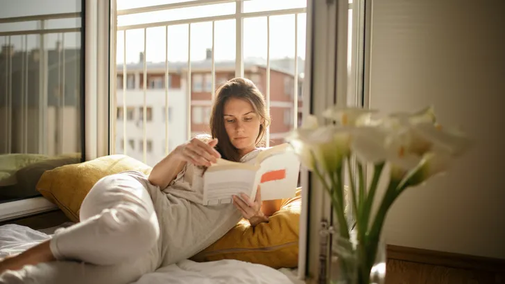 Young woman reading book on bed at home