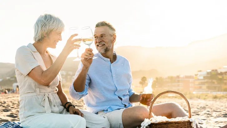 Foto van stel dat samen wijn aan het drinken is op een strand. – Stellen die samen drinken zijn gelukkiger en leven langer volgens onderzoek.