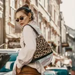 Outdoor autumn fashion portrait of elegant, luxury woman wearing sunglasses, trendy white shirt, leather trousers, with animal, leopard print bag, walking in street of European city. Copy, empty space