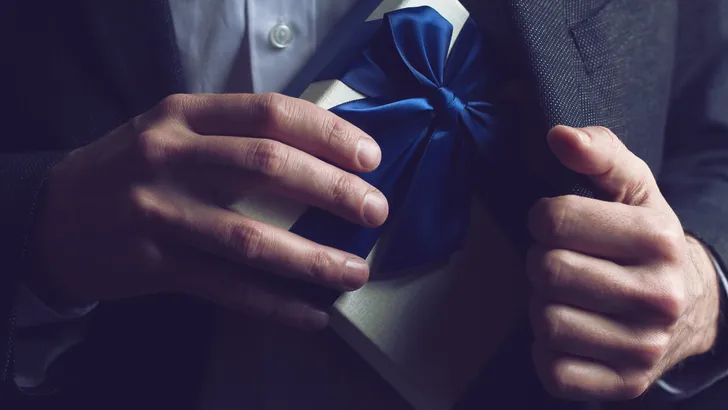 Man in suit opening a gift with blue ribbon