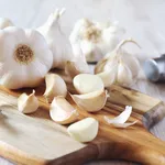 Bulbs of garlic on cutting board and garlic press