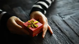 Top view of male and female hands holding gift box with ribbon on wooden background. Present for birthday, valentine day, Christmas, New Year. Congratulations background copy space.