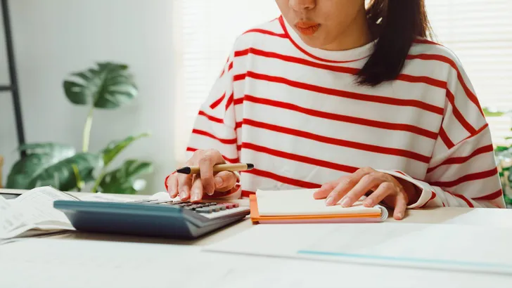 Close-up Young Asian woman with sweater sit front desk with tablet use calculator calculate to utility bills check credit card receipt monthly expense bill at house.