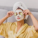 A beautiful young woman gets a face mask in the spa center, lying with cucumbers in her eyes. Happy and gets a lot of fun.