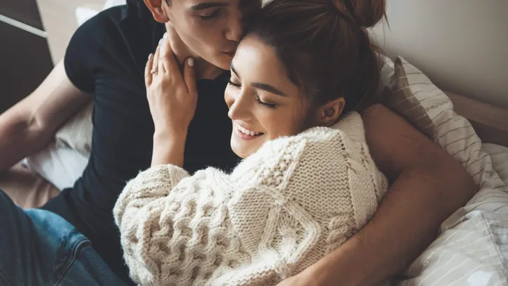 Caucasian man kissing his cute wife dressed in a white knitted sweater embracing in bed