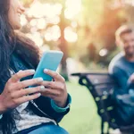 Flirting couple in the park texting on smartphones