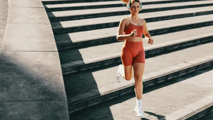 Athletic female using music to enhance running and jogging outdoor stairs workout