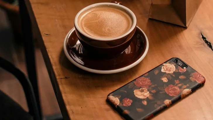 Een telefoon met hoesje en een kop koffie op de tafel