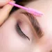 5 tips voor perfecte wenkbrauwen – Close-up van gezicht vrouw met roze borsteltje bij wenkbrauw.