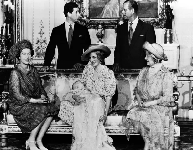 Zwart-wit foto na de doop van prins William in 1982 met William op schoot bij prinses Diana, links koningin Elizabeth en rechts de Queen Mother. Achter de bank staan prins Charles en prins Philip.