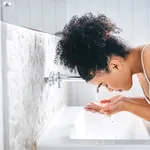 Shot of a young woman washing her face in her bathroom basin