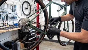 Een fietser met zwarte nitrile handschoenen gebruikt een missing link-tang om een nieuwe, glimmende ketting te installeren op zijn racefiets, die in een montagestandaard hangt in een goed verlichte thuiswerkplaats.