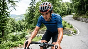 Gefrustreerde mannelijke wielrenner met helm op kijkt zwoegend naar zijn fietscomputer tijdens een steile beklimming.
