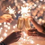 Hands of couple with flutes of champagne and their friends with bengal lights