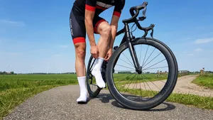 Mannelijke wielrenner staat naast zijn racefiets met hoge carbonwielen en trekt zijn witte aerosokken strak aan voor een rit.
