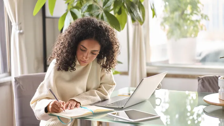 Young woman student using laptop watching online webinar writing at home.