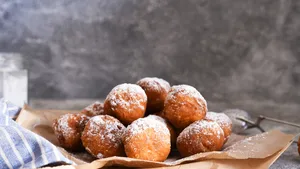 Fried donuts with icing sugar on the kitchen table.