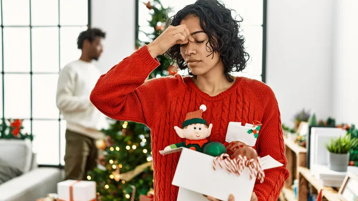 Young hispanic woman standing by christmas tree with decoration tired rubbing nose and eyes feeling fatigue and headache. stress and frustration concept.