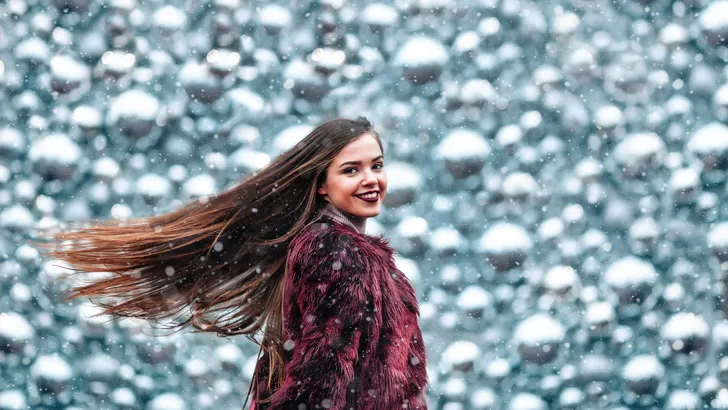 Outdoor close up portrait of young beautiful girl with long hair posing in street of european city. Christmas, winter holidays concept. Snowfall. Hair fluttering in the wind.