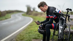 Gefrustreerde wielrenner kijkt naar zijn fietscomputer tijdens een pauze langs de weg, peinzend over zijn training en gewichtsverlies.