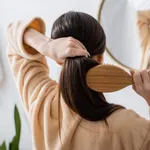 back view of young brunette woman brushing hair in bathroom.