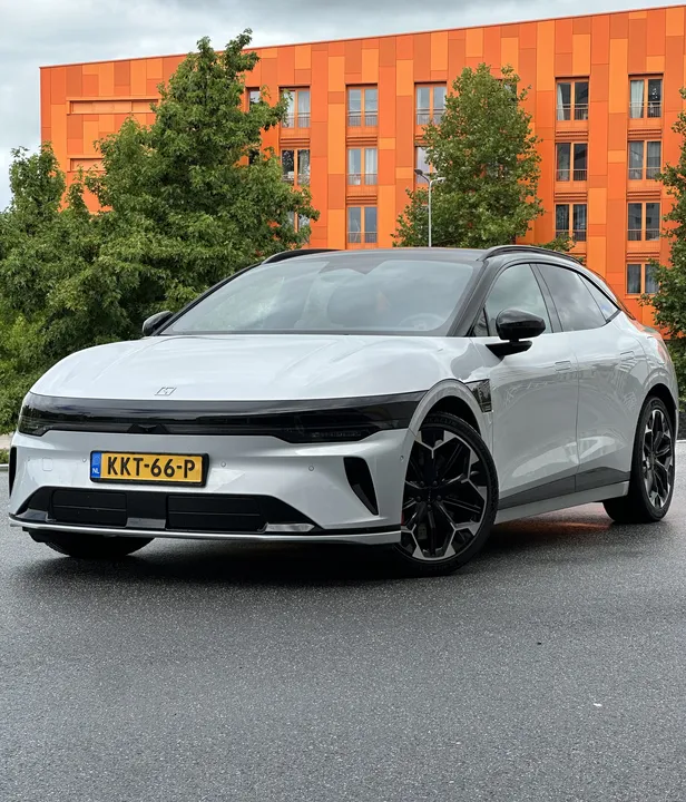 Zeekr 7GT Privilege AWD in Glacier Silver, schuin van voren voor een oranje gebouw op nat wegdek