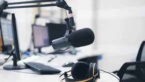 A radio station's live room with a mic stand and headphones on a workbench, digital mixing console and mixing system.