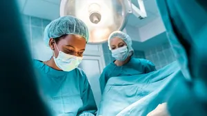 Closeup shot of young adult dedicated black female surgeon concentrated on performing operation standing under the surgical light with female colleague professionally dressed in operating gowns.