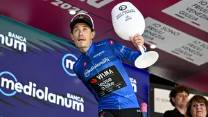 Jonas Vingegaard, in de blauwe trui, wil iets naar het publiek gooien op het podium van de Giro d'italia.