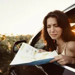 Lost young woman sitting in her car in the countryside and looking at map