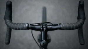 Close-up van een fietsstuur waarbij het slecht gewikkelde stuurlint omhoog krult onder de druk van een natte fietshandschoen.