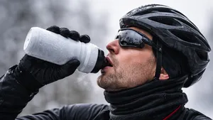 Close-up van een winterfietser die uit een met rijp bedekte bidon drinkt, met zichtbare adem in de koude lucht.
