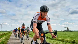 Een mannelijke wielrenner met helm op zijn racefiets die het tempo flink opvoert tijdens een groepsrit in de polder.