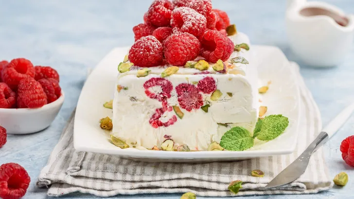 Semifreddo with raspberries and pistachios on a white platter. T