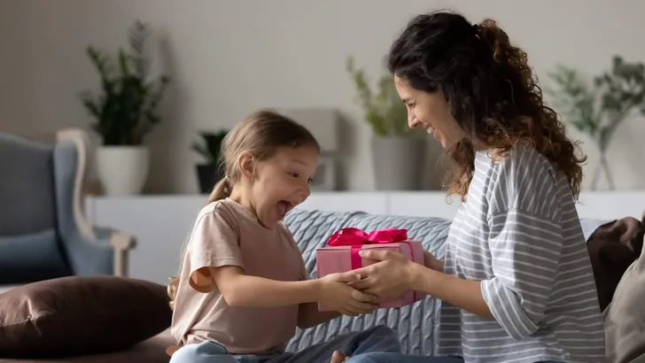 Loving mother giving pink gift box to surprised little daughter