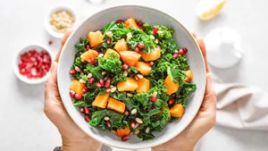 Vegetable salad bowl in woman hands. Fresh kale and baked pumpkin salad. Healthy eating concept