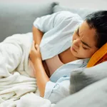 Young Asian woman suffers from stomachache while lying down on sofa at home.