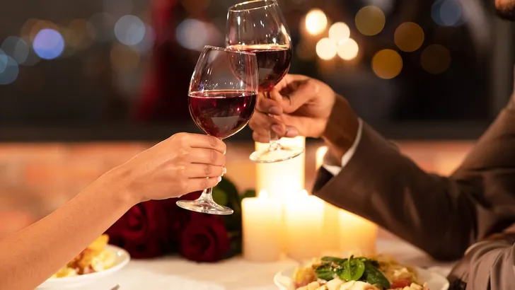 Couple's Hands Clinking Glasses Of Red Wine Dating In Restaurant