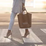 close up of woman legs walking on crosswalk. The woman is wearing shoes on high heels. Handbag in woman hand.