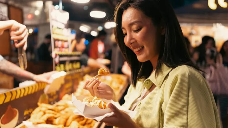 Asian woman enjoy eating fries street food at night market. Trav