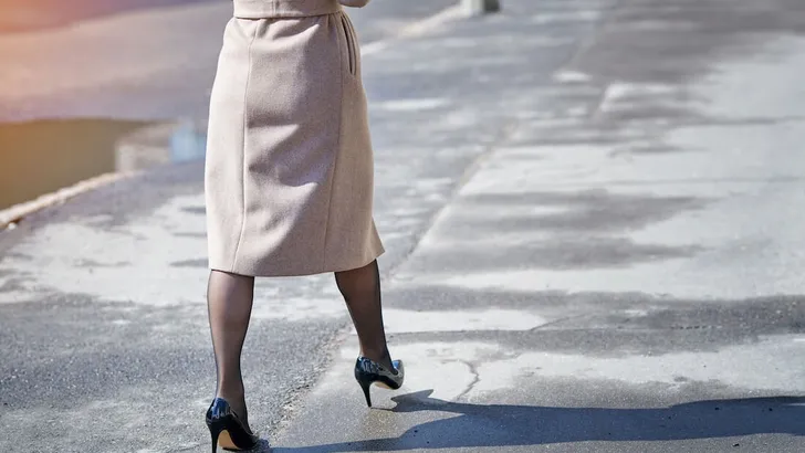 Fashion woman in black patent leather high heels shoes and coat walking on spring city street. Girl with perfect legs in black tight pantyhose. Female feet in shoes on asphalt, elegant woman in coat